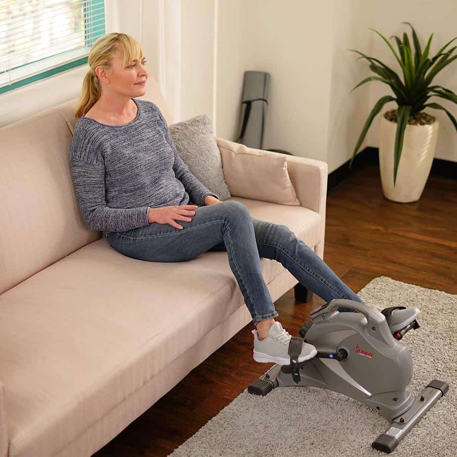 A lady exercising with the Sunny Health & Fitness SF-B0418 Mini Bike while sitting on the sofa