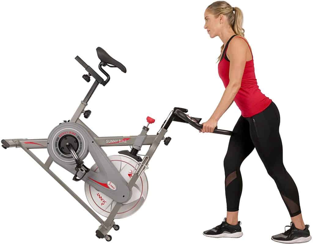 A lady moves the Sunny Health & Fitness Synergy SF-B1879 Indoor Cycling Bike for storage