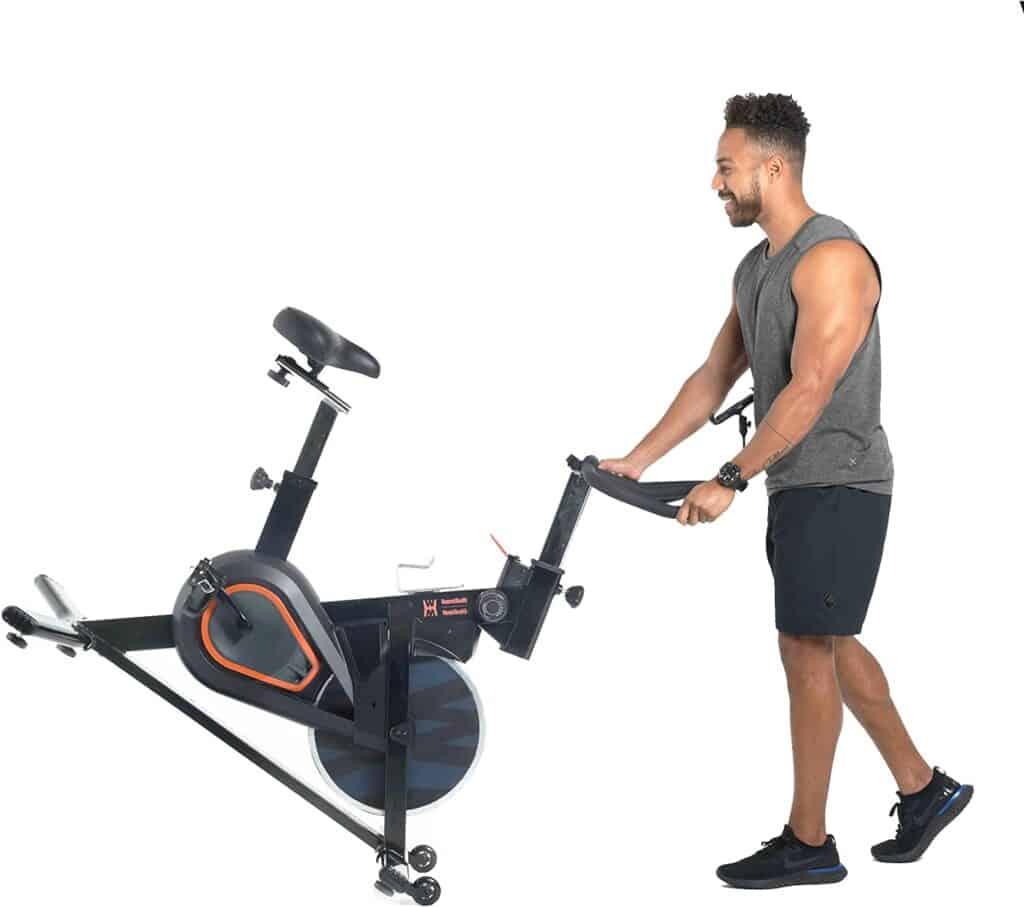 A man moves the Women’s Health Men’s Health Eclipse Indoor Cycling Bike to a storage area.